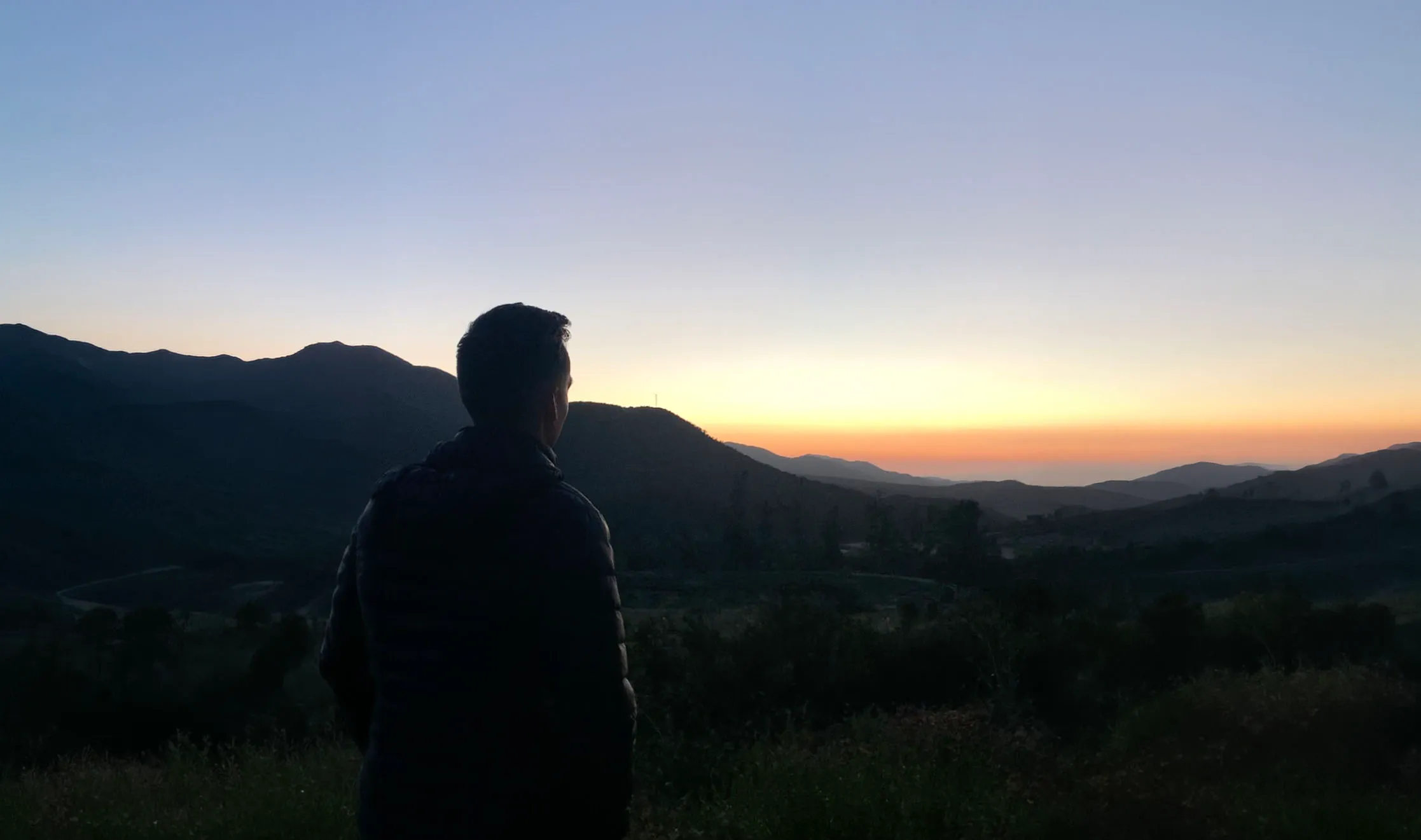 A man in silhouette watching the sunset over a mountain valley